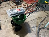 Green Scotts Turf Builder EdgeGuard Mini broadcast seeder assembled, showing plastic hopper and black wheels, with 3 black hook plates wrapped in plastic on top