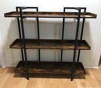 Front view of the three-tier wood shelf with black steel frame on a hardwood floor against a light wall.