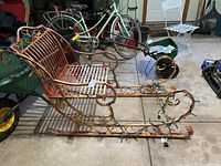 Wrought iron sleigh angled side view showing the curved runner, seat, backrest, and string of Christmas lights attached.