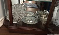 Wide view of the vintage glass tray, bowls and divided dish with silver overlay pattern arranged in a wooden display cabinet.