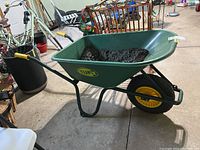 Side view of the green Tufx plastic and metal wheelbarrow with yellow handles and inflatable tire, with some dirt residue inside.