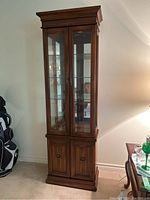 Front view of the full wooden display cabinet showing two glass doors on top and two wooden doors below, standing tall against wall.