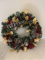 Front view of Christmas wreath showing pinecones, gold holly leaves, and red decorative accents on artificial pine greenery.
