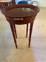 Front view of the round Bombay side table showing the full table and legs with brass handle on the removable tray top