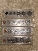 Four sets of Canadian coins from 1976 to 1979 in clear plastic sleeves laid out on carpet.