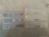 Three Canadian coin sets from 1973, 1974, and 1975 in plastic holders, with paper sleeves labeled with years