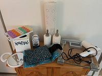 Photo of the lot showing the medication dosette, microwaveable heat pack, soap dispensers, back wrap, non-slip shower pad, hair dryer, and other bathroom items on a wooden surface.