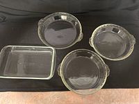 Top view of three circular Pyrex glass baking dishes and one rectangular dish on black fabric background.