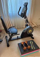 Full view of Gold's Gym stationary bike with padded seat and digital console next to weights and exercise step on carpeted floor