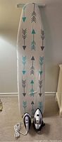 Full view of ironing board with cover featuring teal and black arrow pattern, plus two irons placed in front (Black & Decker and Sunbeam Steam Master)