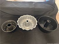 Three fluted tube baking pans of different sizes and colors shown side by side on black backdrop.