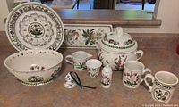 Photo showing entire lot with oval bowl, clock plate, soup tureen, mugs, salt shaker, small bell, creamer, 3 wine glasses, votive holder, and serving board arranged together.