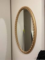 Front angled view of the oval mirror showing detailed ornate gold frame and reflection surface.