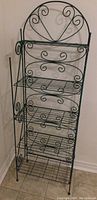 Front view of green metal wire folding rack, showing entire rack with multiple fold-down shelves and decorative scrollwork design.