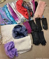 Overview photo showing six pairs of women's gloves mostly black plus purple, assorted colorful scarves including silk and knit, and some other textile items arranged on carpet.