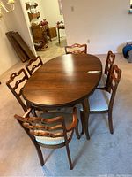 Brown oval dining table with six matching chairs around it, placed on beige carpet.