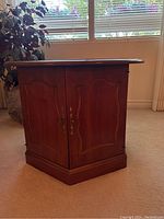 Full view of the wooden side table showing the hexagonal shape, paneled doors, and brass handles