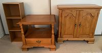 Three wooden furniture pieces shown together: tall cabinet-style side table with double doors, square side table with drawer and bottom shelf, and small open shelf cabinet with three compartments.