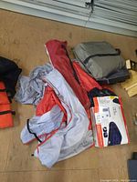 Photo shows the two packed air beds, the opened camping chair bag, and the grey tarp carrying case on the floor.