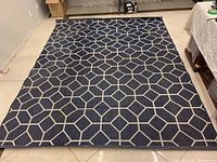 Full view of dark blue outdoor area rug with beige geometric pattern laid out on tile floor.