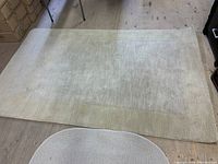 Top down view of beige machine made area rug laid flat on wooden floor, showing overall size and detail of subtle pattern and border.