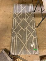 Top-down view of a narrow area rug showing geometric patterns in white on gray background laid on wooden floor.