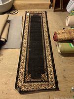 Full view of machine made area rug rolled out on floor, showing overall design and condition including curled edges.