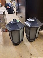 Two hexagonal black and grey lantern-shaped Bluetooth speakers placed on the floor.