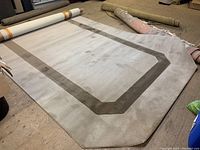 Full image of wool carpet laid flat on floor, showing size and shape with beveled corners and border design.