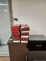 Six red boxes stacked, each holding a doll inside, arranged on a table.