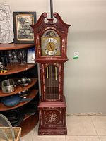 Front view of the full grandfather clock showing the redwood body and mother of pearl inlay with the clock face and glass door.