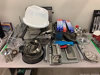 Wide view of kitchenware lot showing Bravetti chafing dish, Pyrex coffee press, metal bowls, graters, and various utensils.