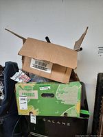 Two cardboard boxes, one green and one brown, with various items stacked inside. Boxes are partially open showing contents.