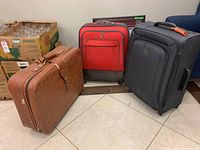 Photo showing three luggage pieces: brown leather-style, red soft shell, black soft shell.