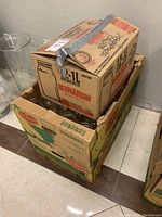 Three stacked cardboard boxes, two banana boxes on bottom and one Bernardin box on top containing mason jars.