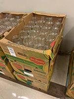 Three cardboard boxes filled with clear glass mason jars without lids. Boxes labeled 'Del Monte Premium Bananas' repurposed for storage. Jars tightly packed in original boxes.