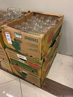 Three stacked cardboard boxes filled with clear mason jars without lids.