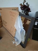 Mirror leaning against wall with original packaging partially visible and nearby golf clubs.
