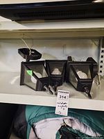 Three black outdoor wall lantern lights with wired bulbs, resting on a shelf.