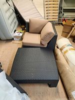 Two black wicker patio chairs with beige cushions, stacked closely indoors with various storage items