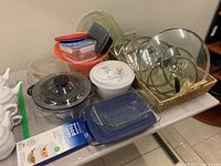 Photo showing a variety of glass lids in a woven basket, along with a white salad spinner, clear glass and colored plastic serving platters, two glass casserole dishes, and plastic storage containers.