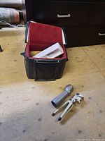 Photo showing the black carrying case with red velvet interior, molded plastic insert, gray telescope, and small tripod placed on a wooden floor.