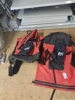 Two red and black waterproof canoe backpacks laid flat on a wooden floor, showing front and top flap with padded shoulder straps.