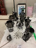 Overview of all seven unique metal wine bottle holders displayed on a table with textured tablecloth