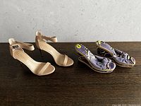 Two pairs of women's shoes side-by-side on a wooden floor; left pair is tan BCBG heels with ankle straps, right pair is periwinkle blue Italian sandals with fabric ruffle details on wedge heels.