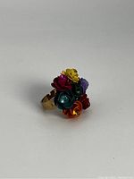 Front angled view of the adjustable ring showing colorful flower design with crystal centers on gold tone metal base.