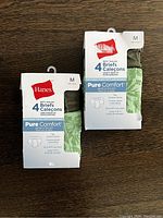 Front view of two packages each containing four medium size boys briefs. Brand Hanes Pure Comfort visible on packaging.