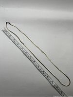 Full length of gold tone chain necklace measured with ruler showing approximately 18 inches length.