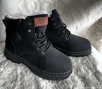 Side angle photo showing the black boots with faux fur lining and 'SPORT FASHION' patch on tongue, thick tread soles, stitched detailing and embossed logo.