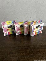 Four new packages of washable sidewalk chalk on a wooden surface against a neutral background. Three packages labeled as neon colors and one as glitter.